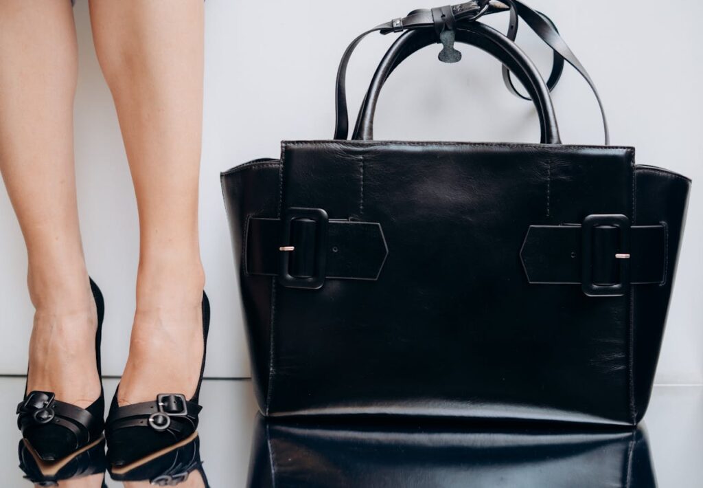 Sophisticated black leather handbag paired with elegant high-heel shoes against a white background.