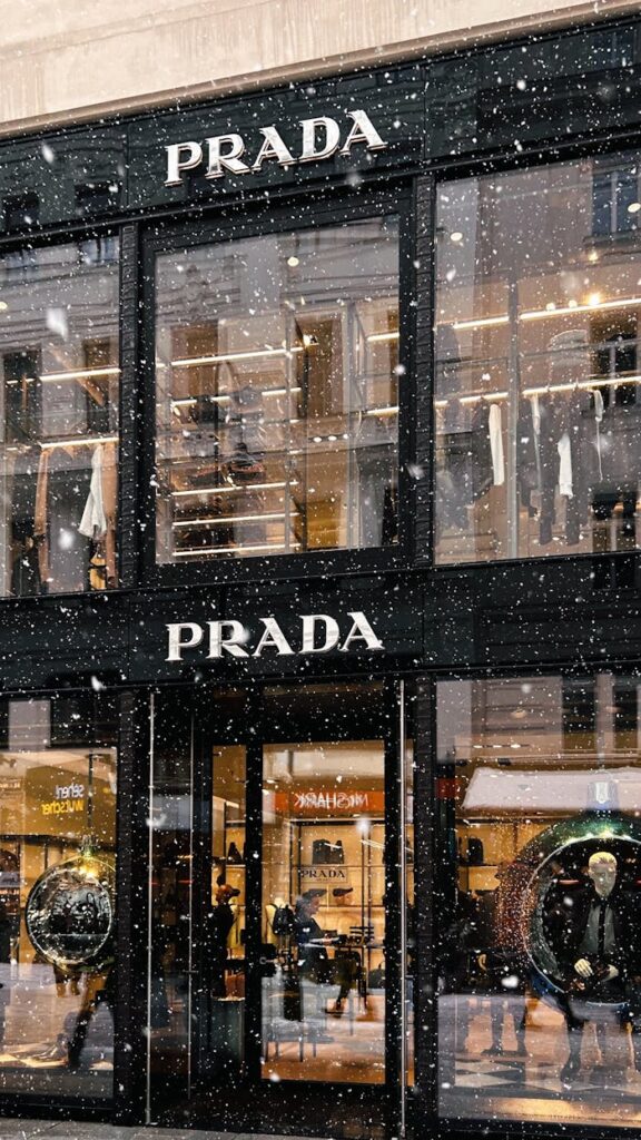 Captivating snowfall at Prada storefront, showcasing fashion during winter.