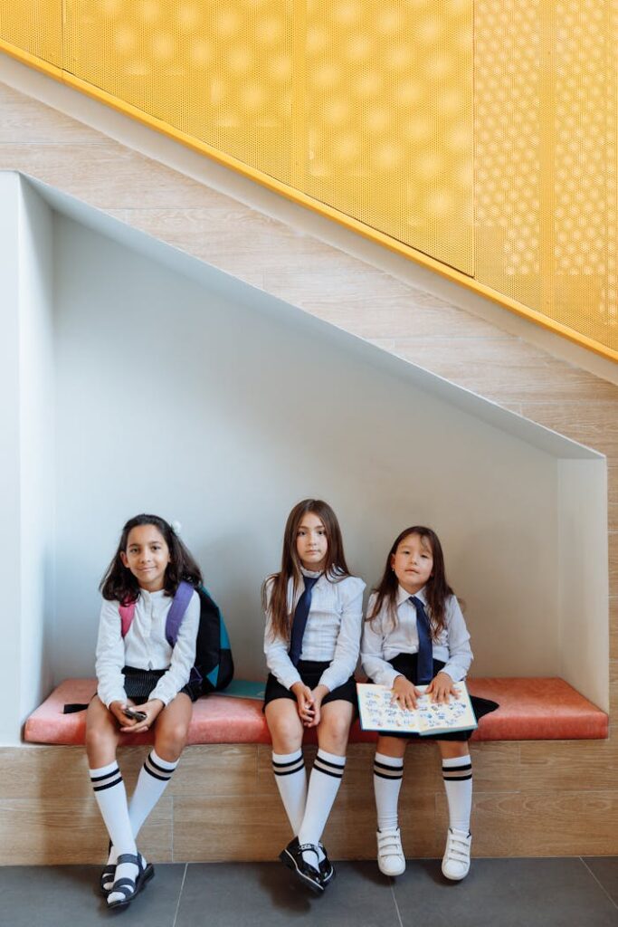 Three schoolgirls in uniforms sit together on a bench indoors.